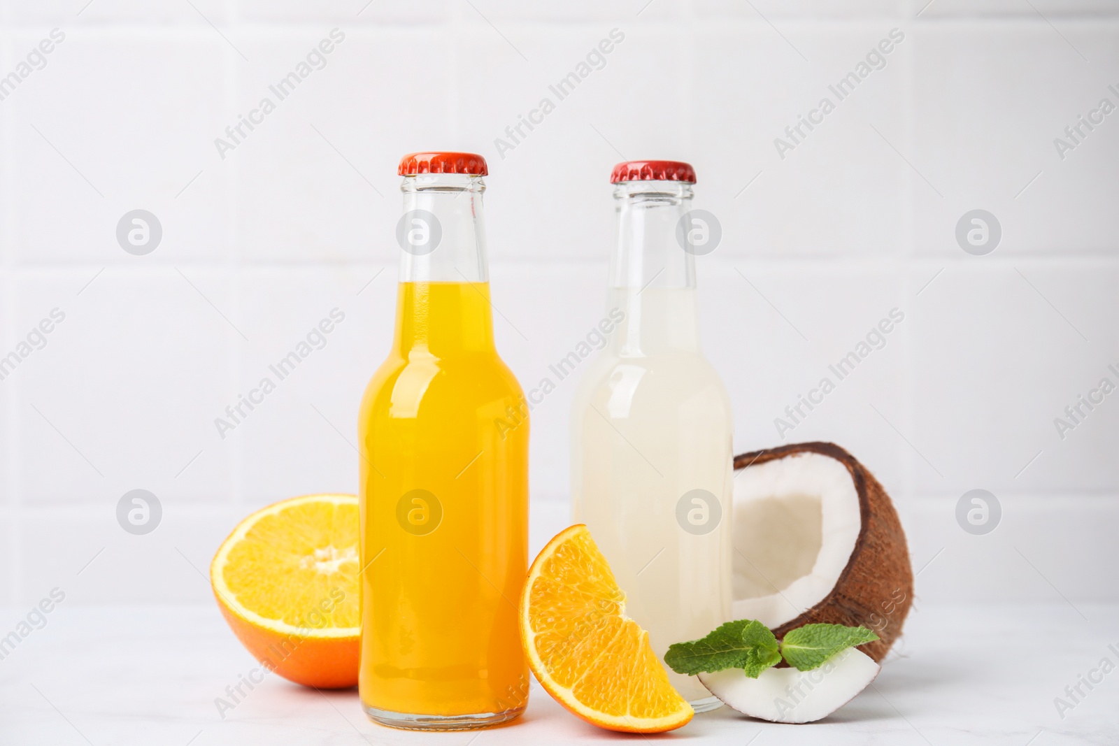 Photo of Delicious kombucha in glass bottles, orange, coconut and mint on white table