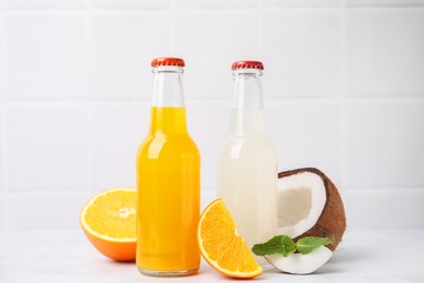 Photo of Delicious kombucha in glass bottles, orange, coconut and mint on white table