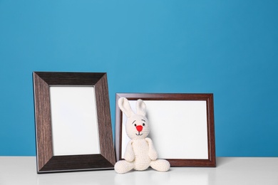 Photo of Photo frames and adorable toy bunny on table against color background, space for text. Child room elements