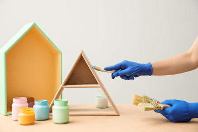 Decorator painting pyramid shaped shelf with brush at wooden table, closeup. Interior element