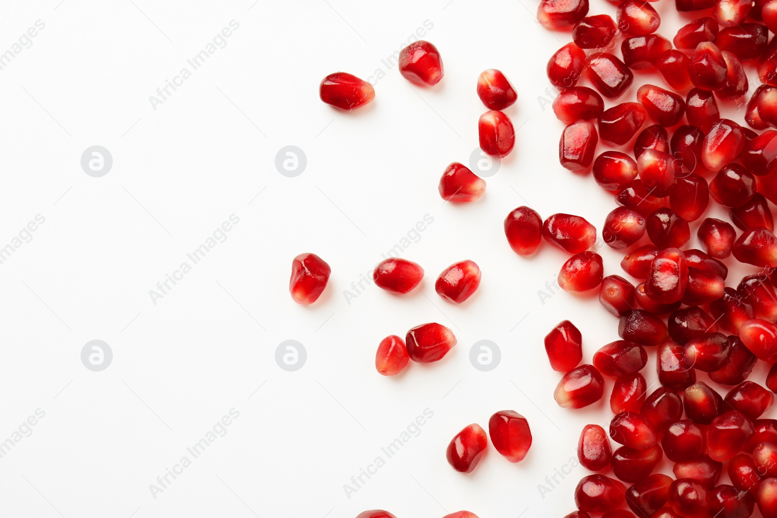 Photo of Many ripe juicy pomegranate grains on white background, flat lay. Space for text