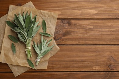 Photo of Fresh green sage with parchment on wooden table, flat lay. Space for text