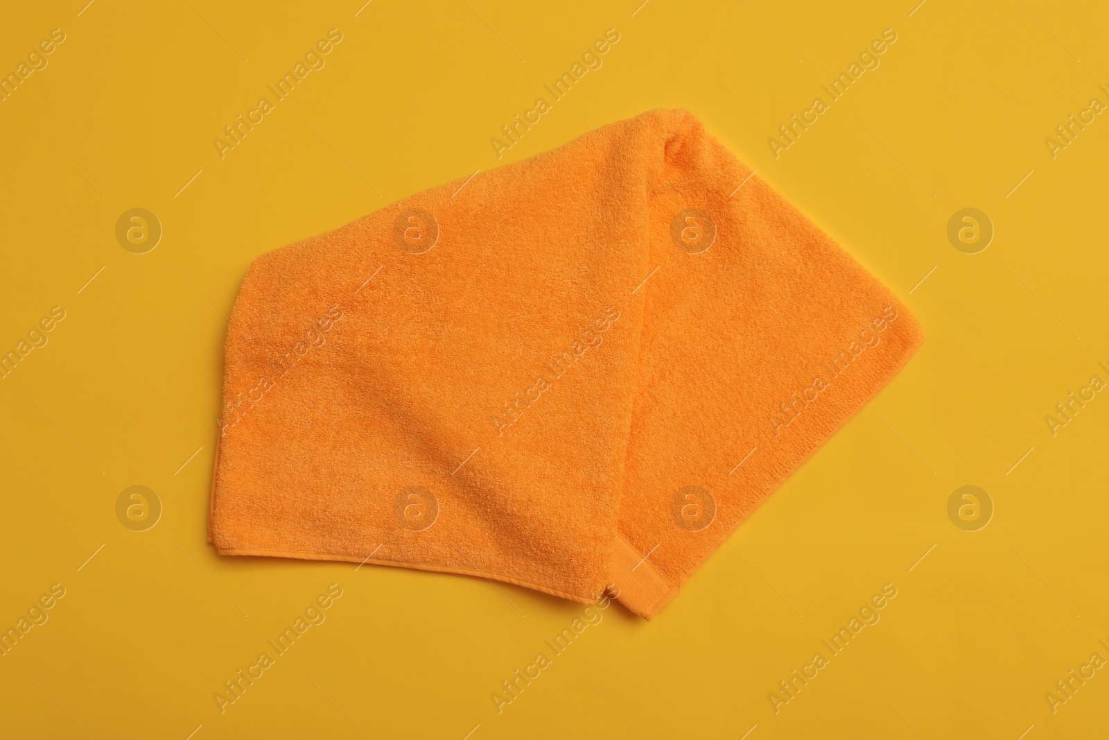 Photo of Folded orange beach towel on yellow background, top view