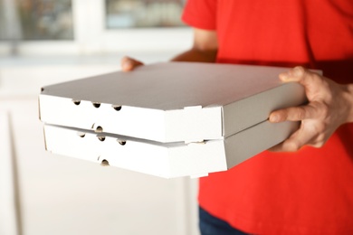 Photo of Young man with pizza boxes indoors, closeup. Food delivery service