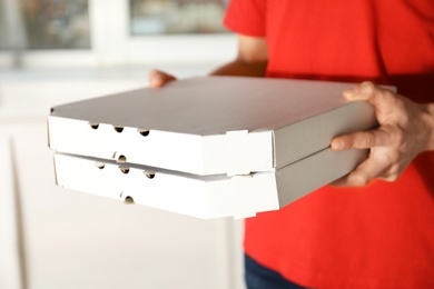 Young man with pizza boxes indoors, closeup. Food delivery service