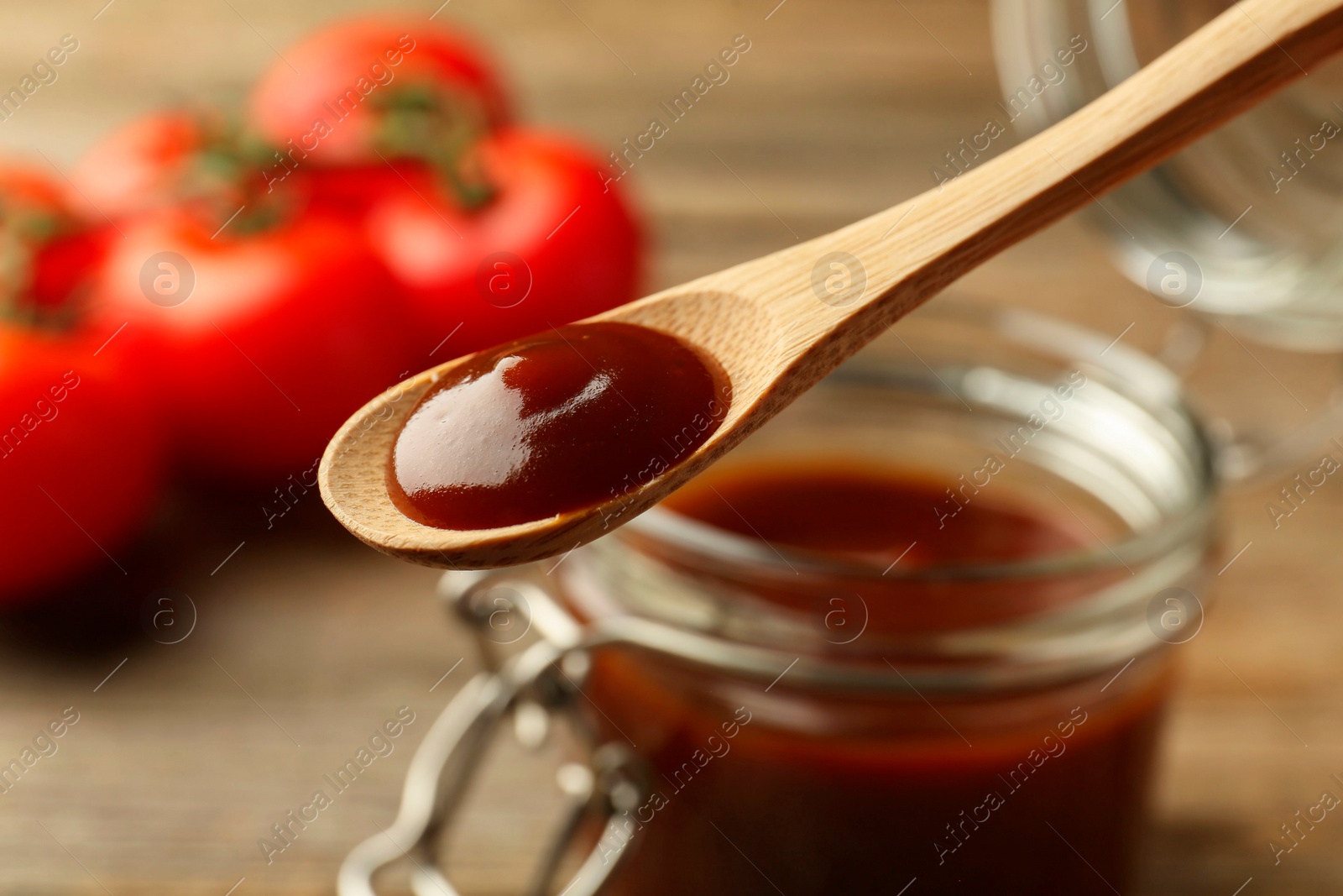 Photo of Taking tasty barbeque sauce from jar with spoon at table, closeup