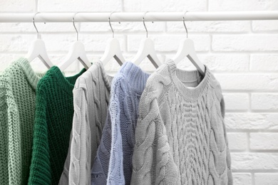 Collection of warm sweaters hanging on rack near brick wall