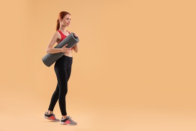 Photo of Young woman in sportswear with fitness mat on beige background, space for text