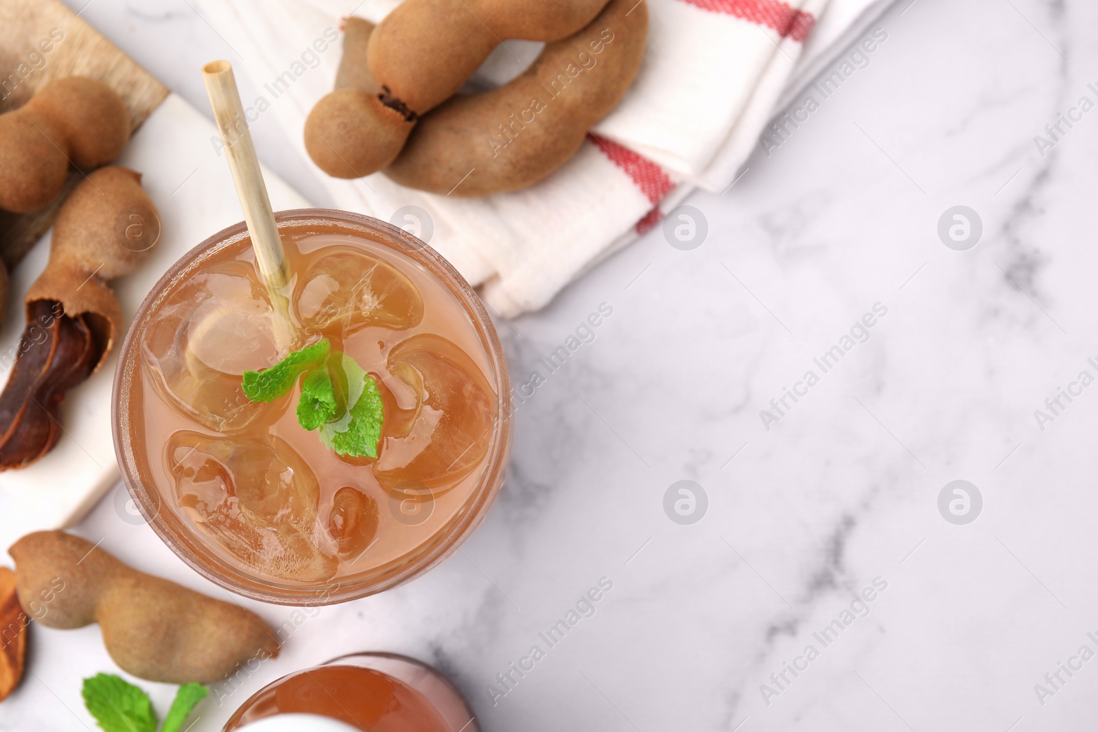 Photo of Tamarind juice and fresh fruits on white marble table, flat lay. Space for text