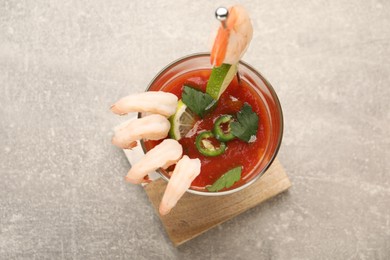 Photo of Tasty shrimp cocktail with sauce, parsley and lime in glass on light grey table, top view