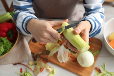 Photo of Woman peeling fresh zucchini with knife at white table, closeup