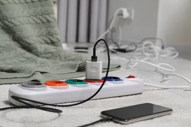 Photo of Extension cord with charger on white floor indoors, closeup