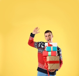 Photo of Happy man in Christmas sweater holding gift boxes on yellow background