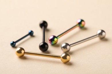 Photo of Different stylish barbells on beige background, closeup. Piercing jewelry