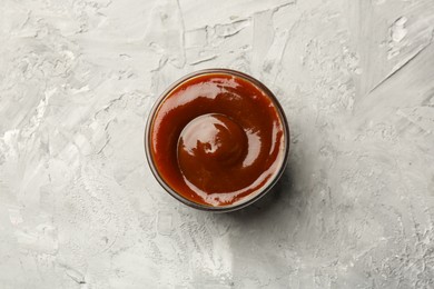 Tasty barbeque sauce in bowl on grey textured table, top view