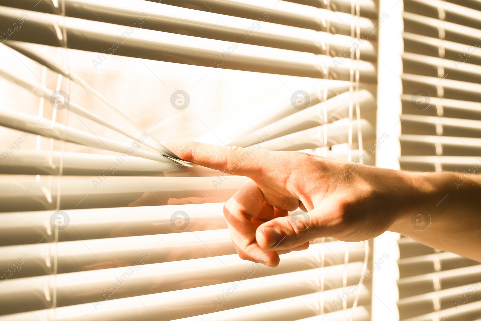 Photo of Man separating slats of white blinds indoors, closeup