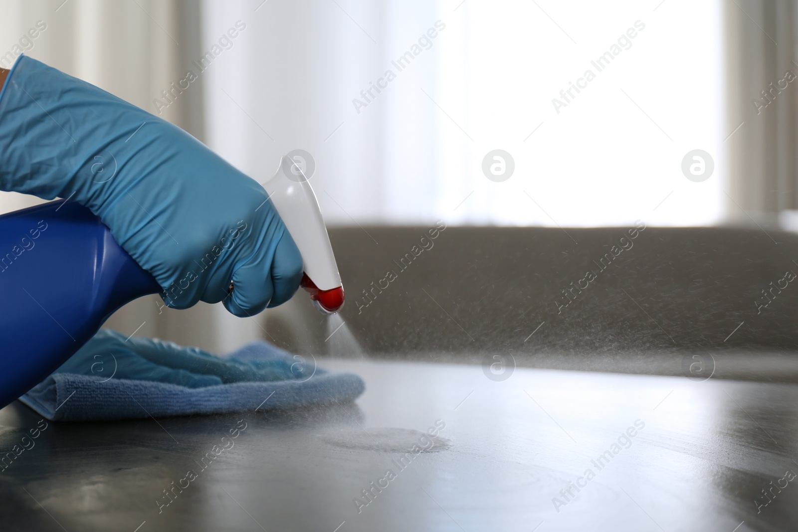 Photo of Woman in gloves cleaning grey stone table with rag and detergent indoors, closeup. Space for text