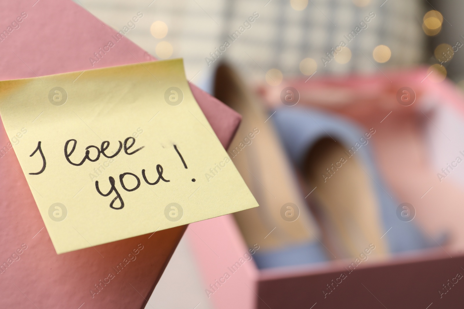 Photo of Note with phrase I Love You attached to cover of shoes box, closeup. Space for text