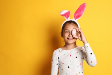 Photo of Cute happy girl with bunny ears and Easter egg against yellow background. Space for text