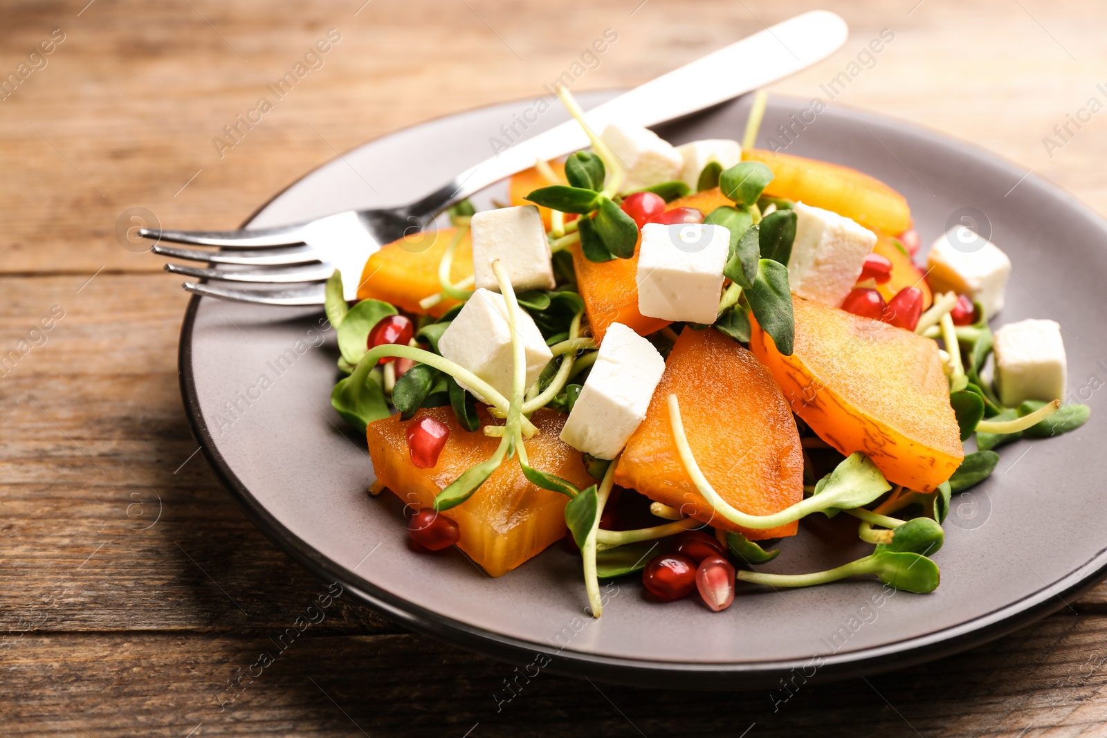 Photo of Delicious persimmon salad served on wooden table, closeup