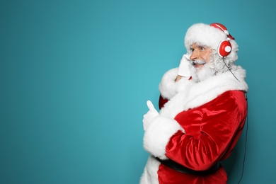 Santa Claus listening to Christmas music on color background