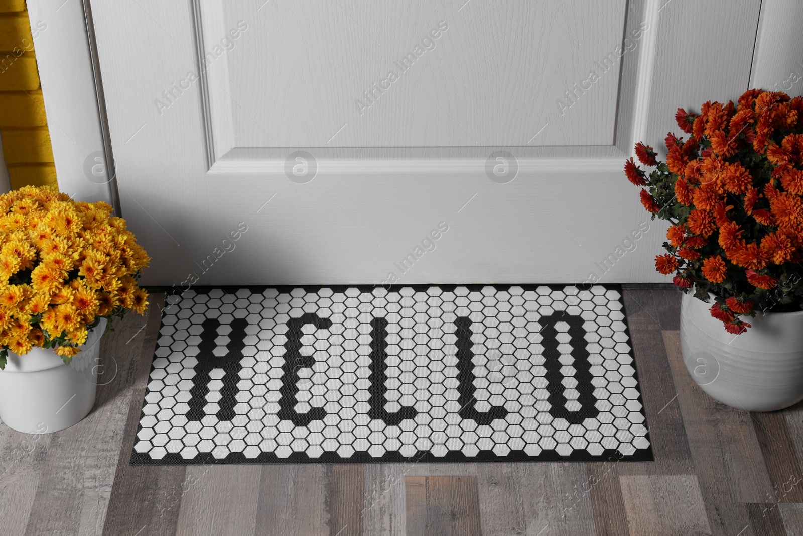 Photo of Stylish door mat with word Hello and beautiful flowers on wooden floor