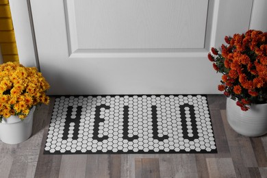 Photo of Stylish door mat with word Hello and beautiful flowers on wooden floor