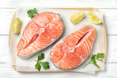 Photo of Fresh raw salmon with parsley and lime on white wooden table, top view. Fish delicacy