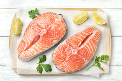 Fresh raw salmon with parsley and lime on white wooden table, top view. Fish delicacy