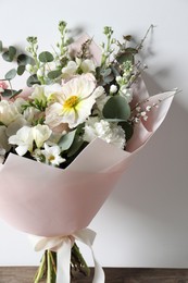 Photo of Bouquet of beautiful flowers on wooden table against white wall