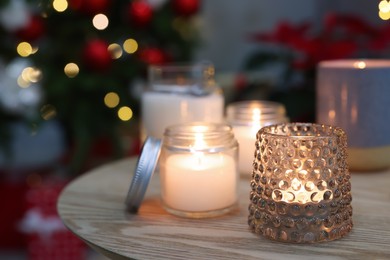 Burning candles on wooden table in room decorated for Christmas