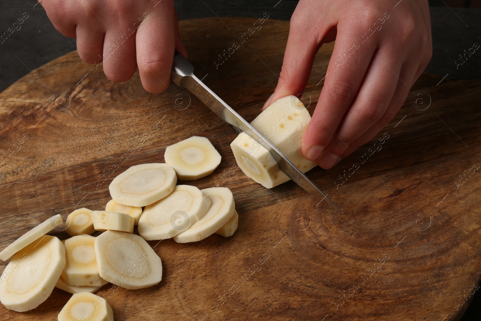 Photo of Woman cutting delicious fresh ripe parsnip at wooden board, closeup