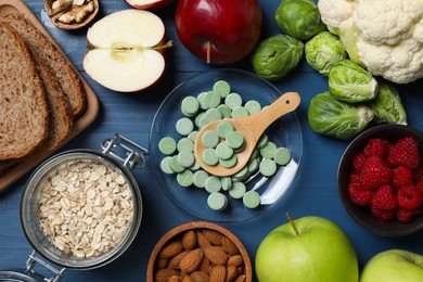 Photo of Bowl with pills and foodstuff on blue wooden table, flat lay. Prebiotic supplements