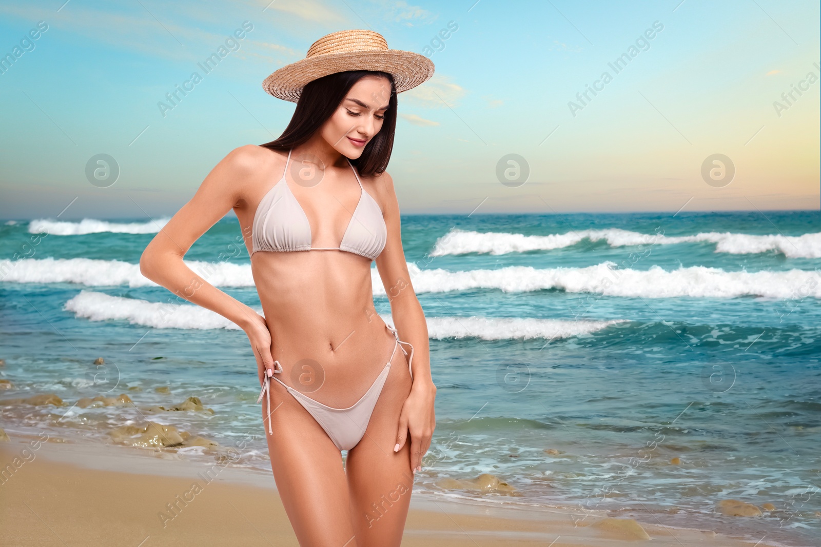 Image of Beautiful woman in stylish bikini and hat on sandy beach near sea, space for text