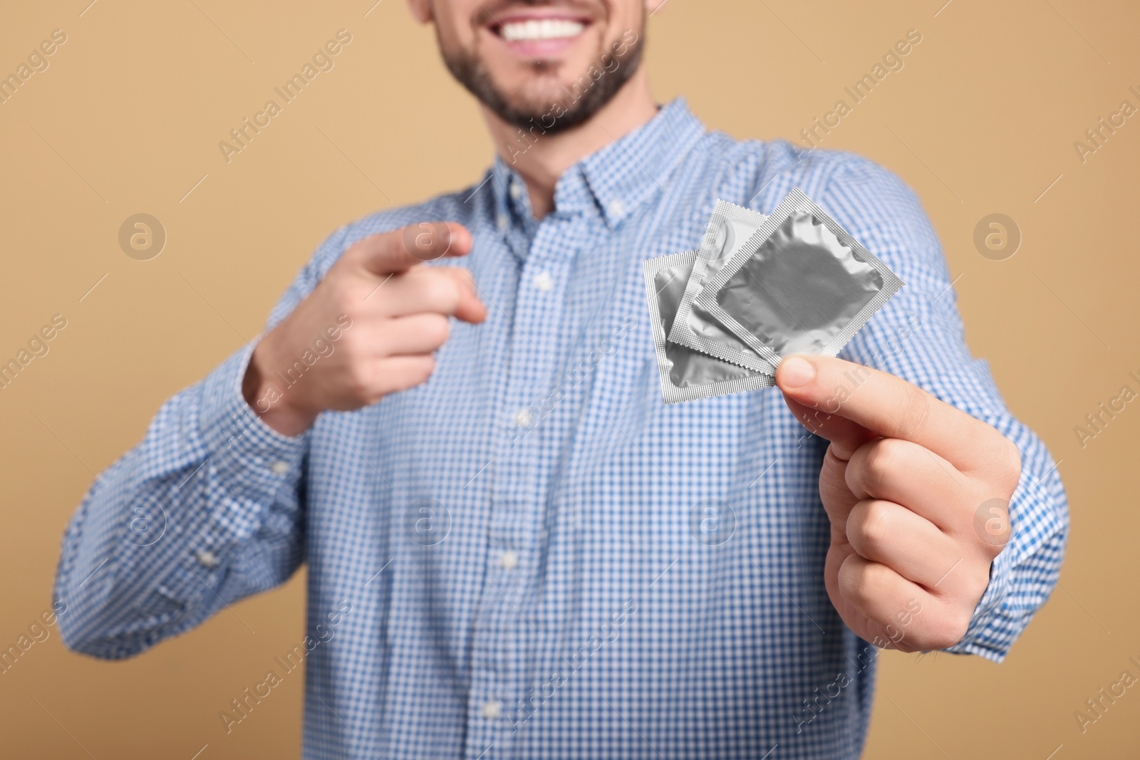 Photo of Happy man holding condoms on beige background, closeup