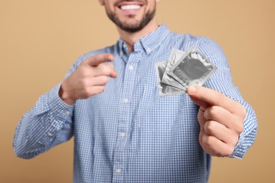 Photo of Happy man holding condoms on beige background, closeup