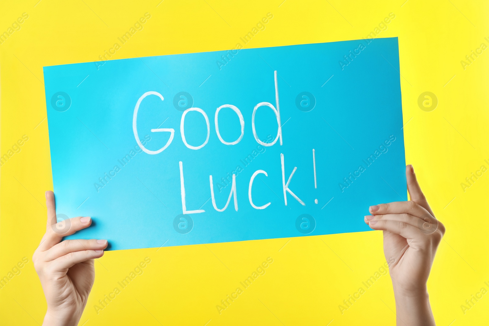 Photo of Woman holding light blue card with words GOOD LUCK on yellow background, closeup