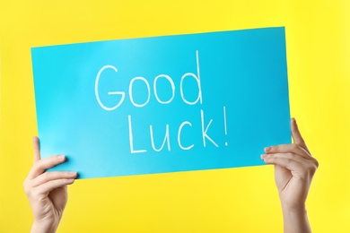 Woman holding light blue card with words GOOD LUCK on yellow background, closeup