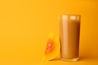 Photo of Tasty pumpkin juice in glass and cut pumpkin on orange background. Space for text