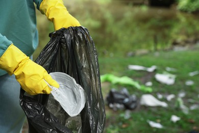 Photo of Woman with plastic bag collecting garbage in park, closeup. Space for text