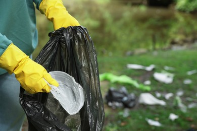 Woman with plastic bag collecting garbage in park, closeup. Space for text