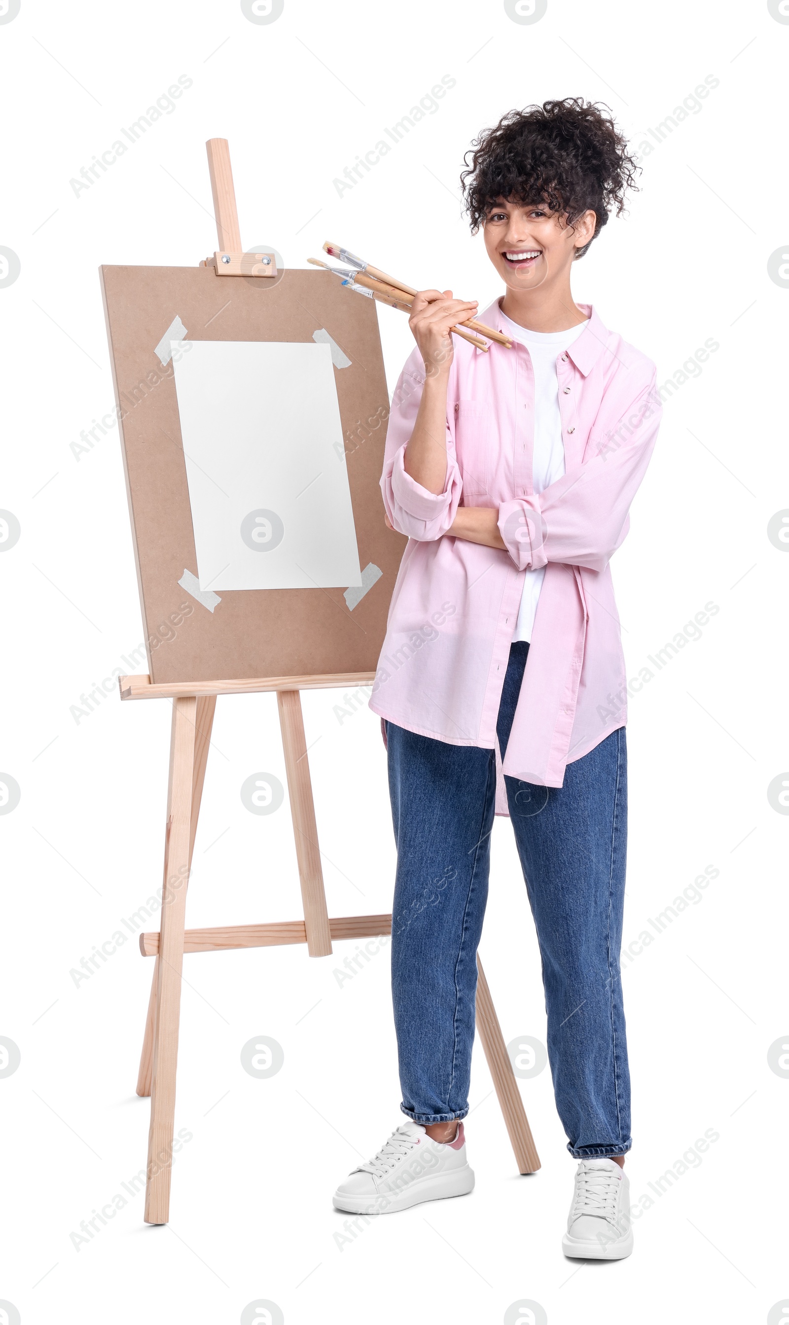 Photo of Young woman holding brushes near easel against white background