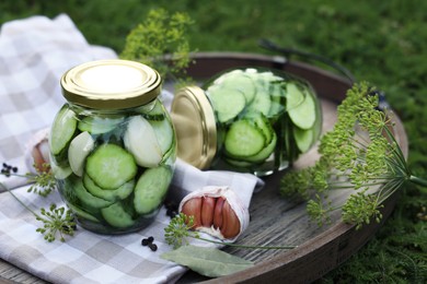 Photo of Jar of delicious pickled cucumbers on wooden tray outdoors, closeup. Space for text