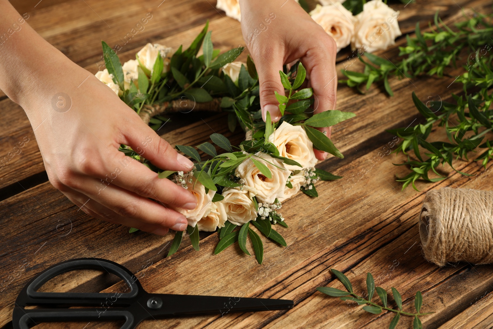 Photo of Woman making wreath of beautiful flowers at wooden table, closeup