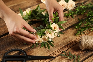 Woman making wreath of beautiful flowers at wooden table, closeup