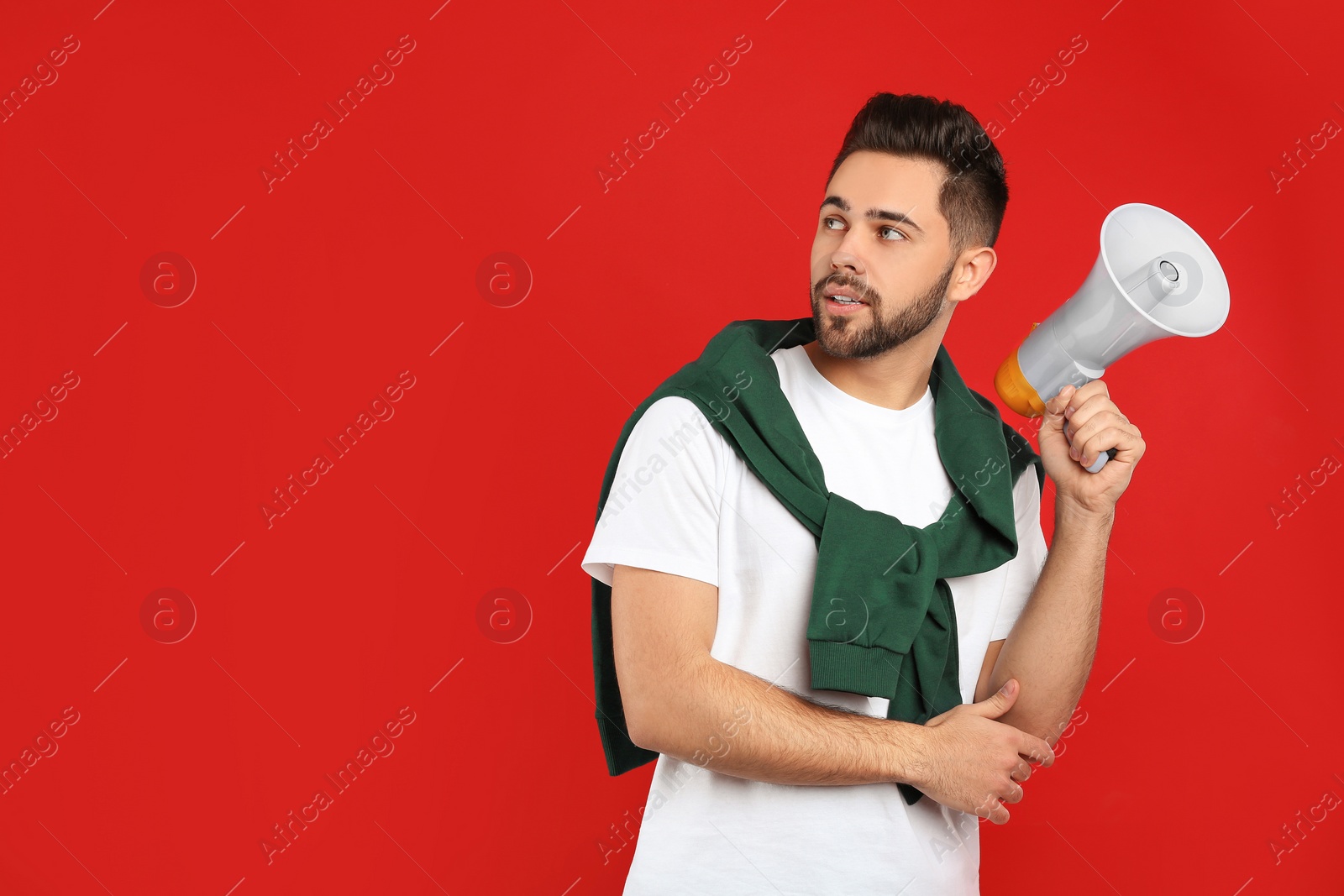 Photo of Young man with megaphone on red background. Space for text