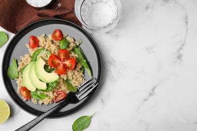 Delicious quinoa salad with tomatoes, avocado slices and spinach leaves served on white marble table, flat lay. Space for text