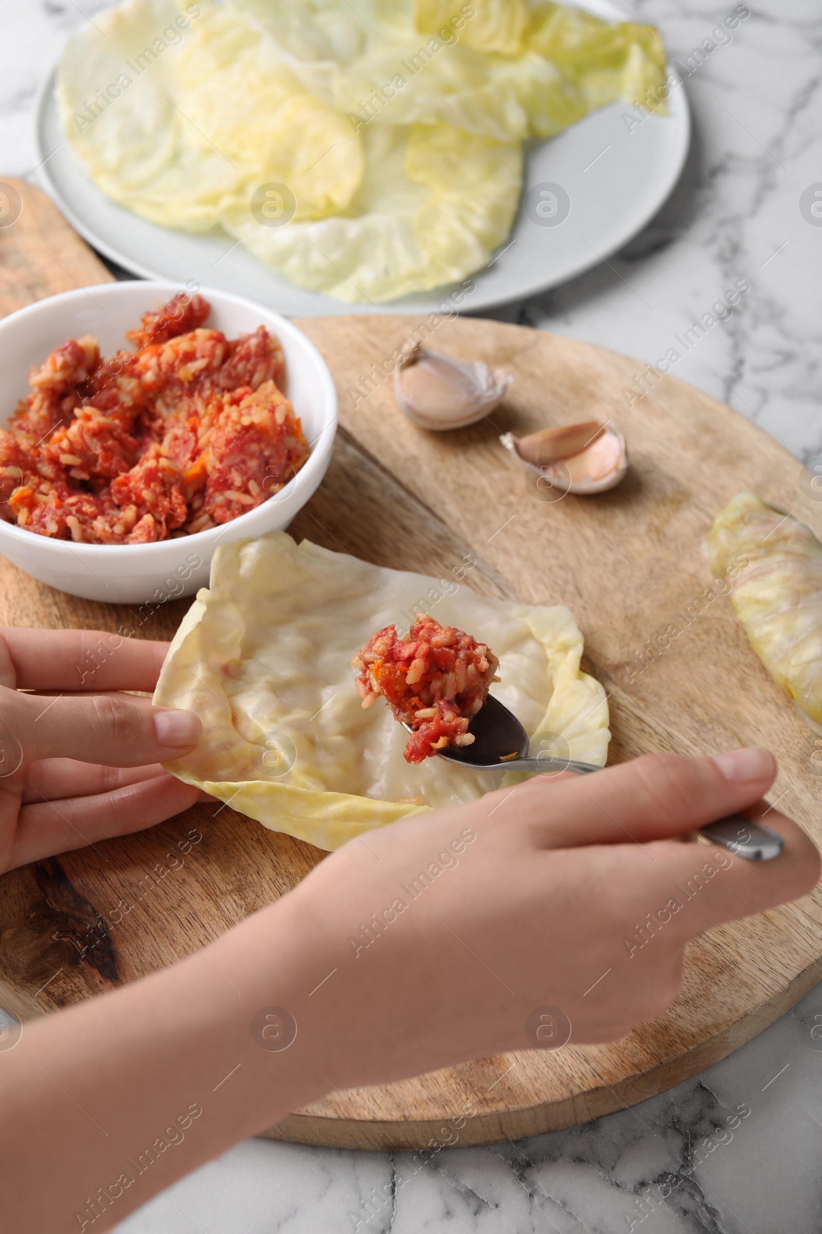 Photo of Woman preparing stuffed cabbage roll at white marble table, closeup