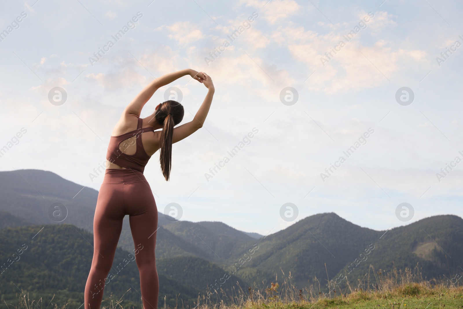 Photo of Woman doing morning exercise in mountains, back view. Space for text