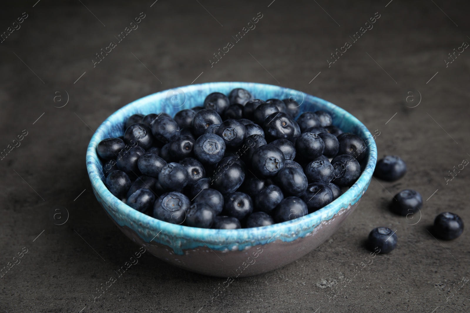 Photo of Bowl of tasty blueberries on grey table